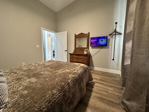 A bedroom with a bed, a dresser, a television, and a door leading to another room. - NEW Creekside Home with Dock, Boat Ramp, and Hot Tub (Gallipolis)