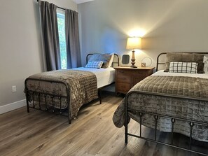 A bedroom with two single beds, a bedside table with a lamp, and a window with curtains.