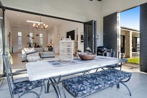 An outdoor patio with a table, bench, and grill area. - Te Puna 5BR Estate | Pool, Tennis, Sauna, Cottage (Tauranga)