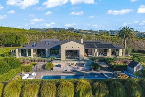 A modern house with a large front porch, a swimming pool, and a view of the surrounding landscape. - Te Puna 5BR Estate | Pool, Tennis, Sauna, Cottage (Tauranga)