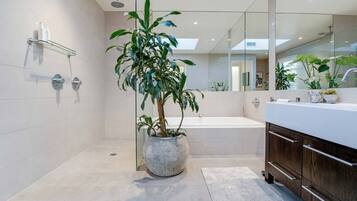 Un baño moderno con un espejo grande, una bañera, una ducha y una planta en maceta.