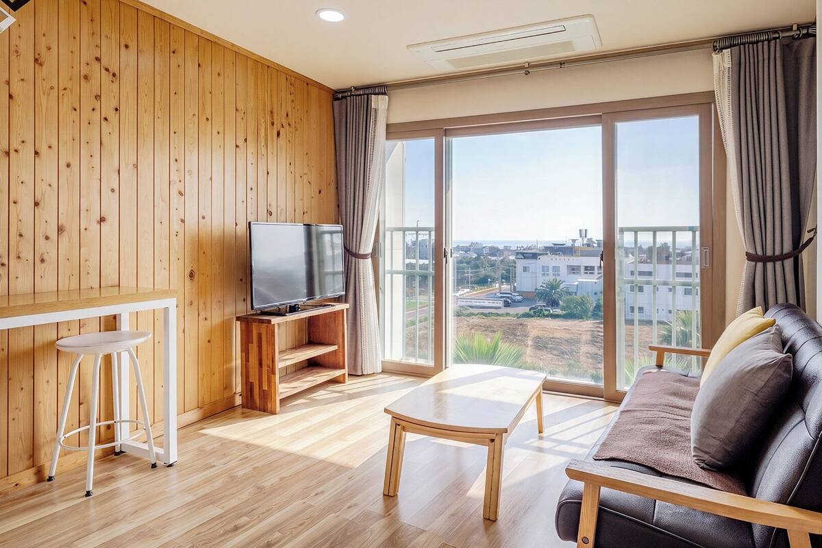 A wooden-paneled room with a TV, bar stools, a sofa, and a table.