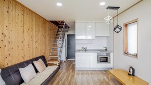 Un espacio habitable compacto con sofá, zona de cocina, escalera y ventana con persianas.