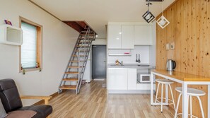 Una cocina compacta con armarios blancos, una escalera de madera y un comedor con taburetes.