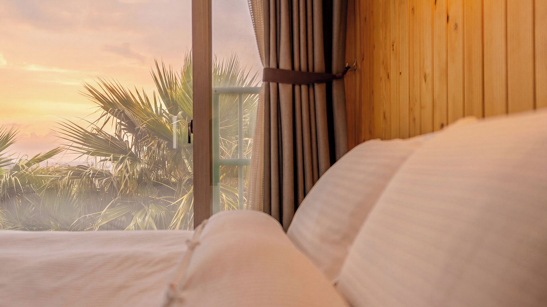 Ein Schlafzimmer mit Blick auf Palmen und einen Sonnenuntergang durch ein Fenster.