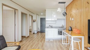 Una cuina moderna amb armaris blancs, un taulell de fusta i un brollador. Hi ha una zona de menjador amb una taula i cadires.