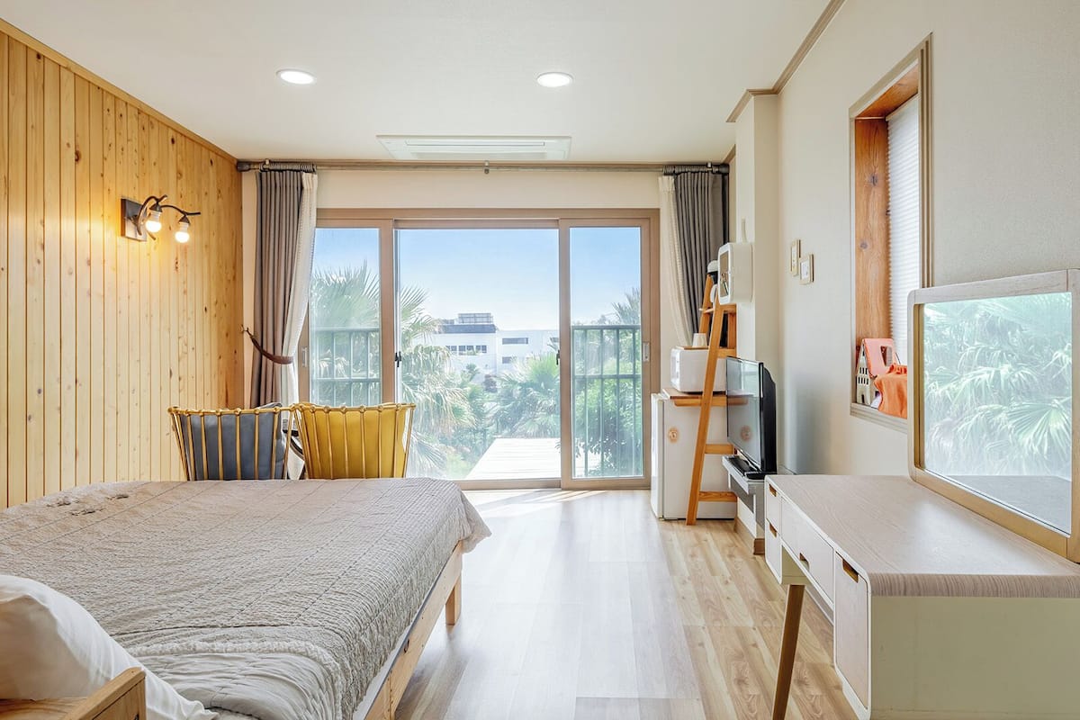 A hotel room with a bed, a desk, a TV, and a balcony with a view.