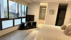 A bedroom with a bed, a TV on a stand, a window, and a door leading to a bathroom. - 70ft from the Tiffany's store in Polanco, near the World Cup, 2-bedroom apartment with a balcony. (Ciudad de México)