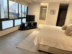 Ein Schlafzimmer mit einem Bett, einem Fernseher auf einem Schrank, einem Fenster und einer Tür, die ins Badezimmer führt.