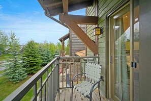 Eine Holzterrasse mit Metallgeländer, einem grünen Stuhl und einer Glastür mit Fenster.
