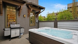 Un jacuzzi al aire libre cerca de una casa, con una parrilla y un carrito.