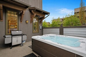 Een bubbelbad buiten een huis, met een barbecue en een karretje in de buurt.