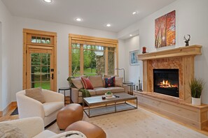 Ein Wohnzimmer mit Kamin, einer Couch, einem Couchtisch und großen Fenstern.