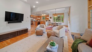 Un espacio habitable amplio con una televisión de pantalla plana, asientos cómodos, una cocina al fondo y ventanas grandes.