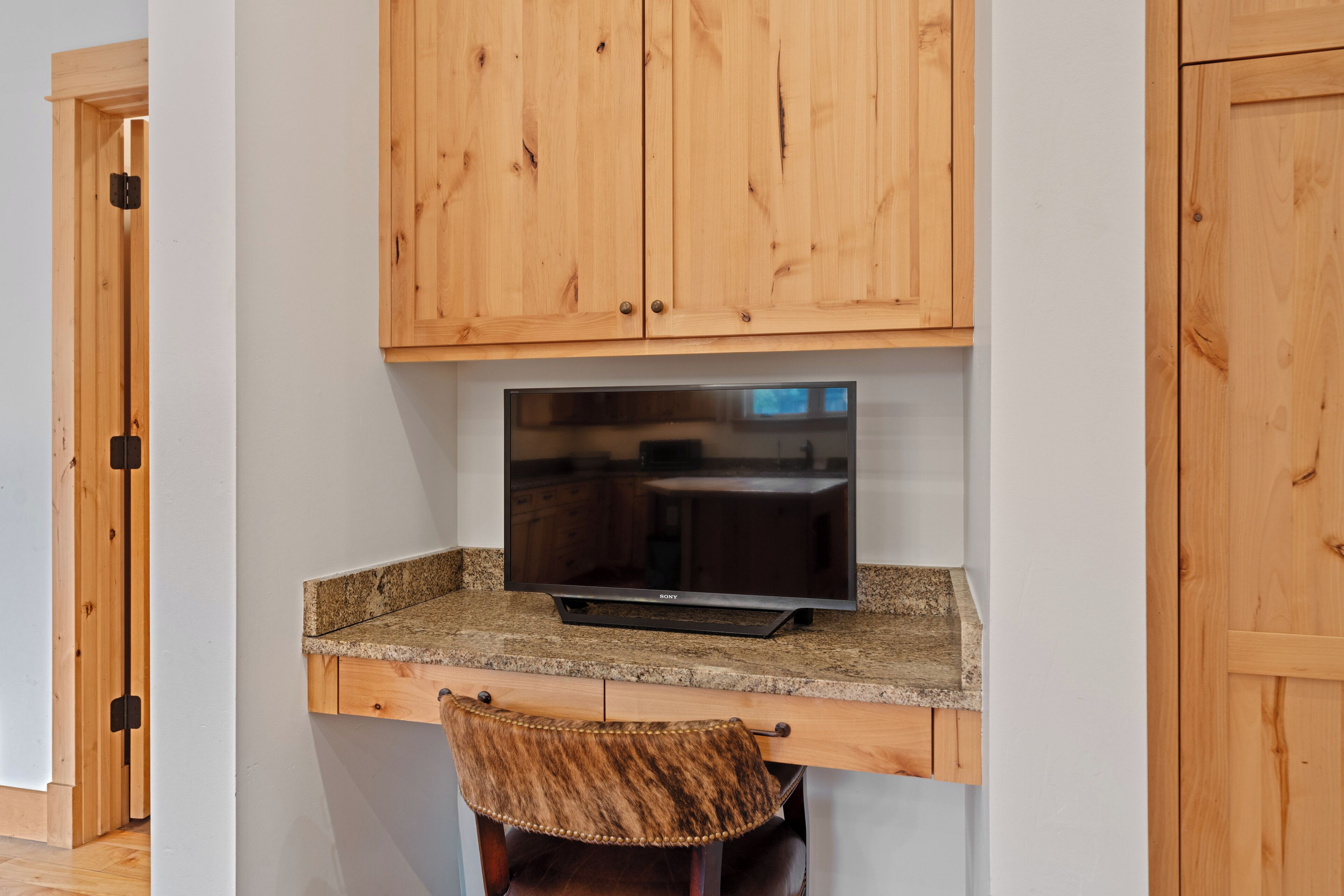 A kitchen with wooden cabinets, a granite countertop, a built-in TV, and a bar stool.