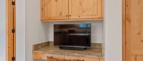 A kitchen with wooden cabinets, a granite countertop, a built-in TV, and a bar stool.