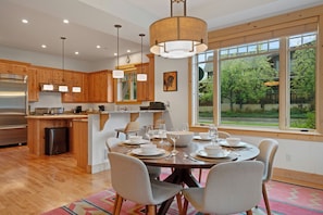 A modern kitchen with wooden cabinets, a stainless steel refrigerator, and a dining area with a round table set for four. - Town Center Home with Private Hot Tub (Gallatin Gateway)