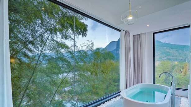 Ein modernes Badezimmer mit einer freistehenden Badewanne, großen Fenstern und Blick auf eine gebirgige Landschaft.