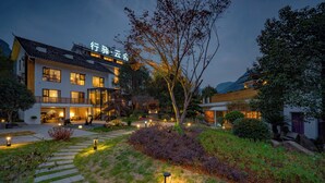 Ein Hotel im traditionellen Baustil, mit einem gut beleuchteten Eingangsbereich, einem Kiesweg und einer angelegten Gartenanlage.