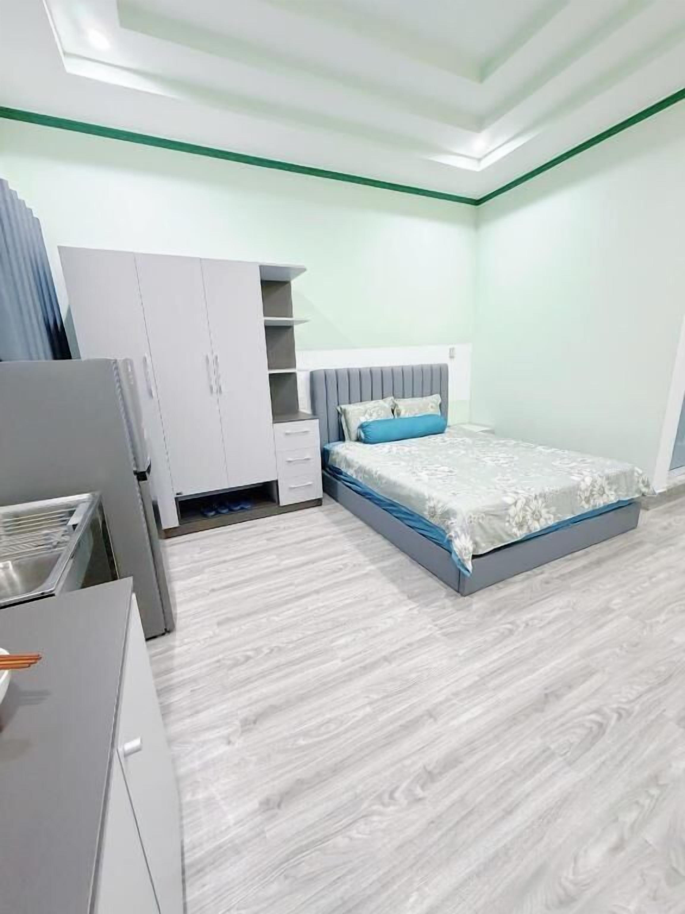 A bedroom with a bed, a wardrobe, a desk, and a kitchenette.