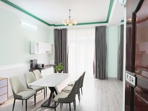 A modern hotel room with a dining area, a kitchenette, and a large window with curtains. - Minihouse 365 holdings Ly Hong Thanh (Cai Khe)