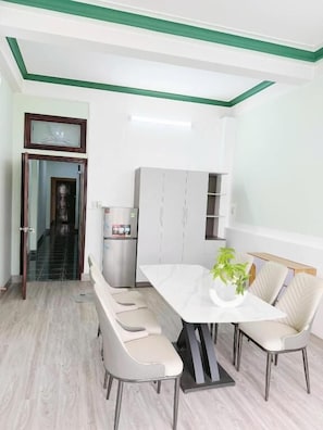 Uma sala de jantar com uma mesa branca, quatro cadeiras, um refrigerador e um armário.