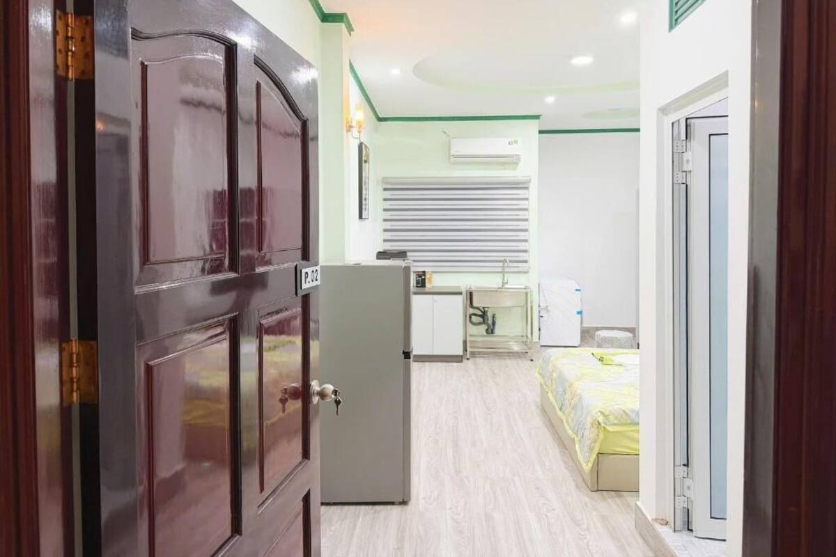 Habitación de hotel con puerta de madera, una pequeña kitchenette, cama y ventana con persianas.