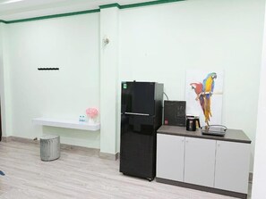 Ein Zimmer mit einem schwarzen Kühlschrank, einem weißen Schrank, einer kleinen Mülltonne und einem Regal mit rosa Blumen.