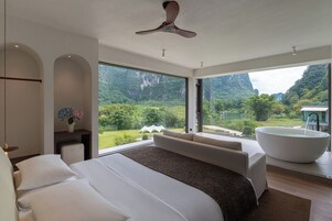 Un dormitorio moderno con una cama grande, un ventilador de techo y vistas a un paisaje montañoso a través de amplios ventanales.
