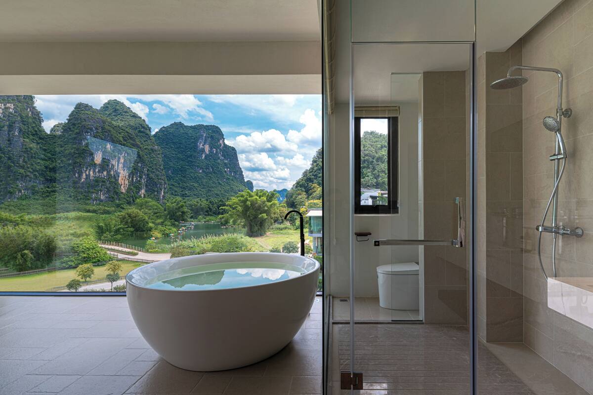 Ein modernes Badezimmer mit einer großen Badewanne, einer Duschkabine aus Glas und Blick auf eine Berglandschaft.