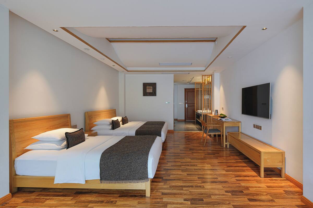 Ein Hotelzimmer mit zwei Betten, einem Schreibtisch, einem Fernseher und Holzboden.