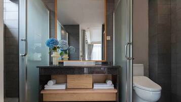 A modern bathroom with a glass shower enclosure, a wooden vanity, a white toilet, and a large mirror.