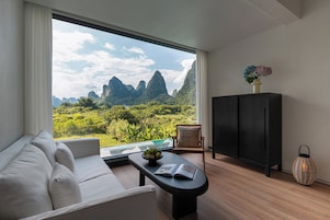 Una habitación moderna con sofá, una mesa con un libro, un armario y vistas a un paisaje montañoso.