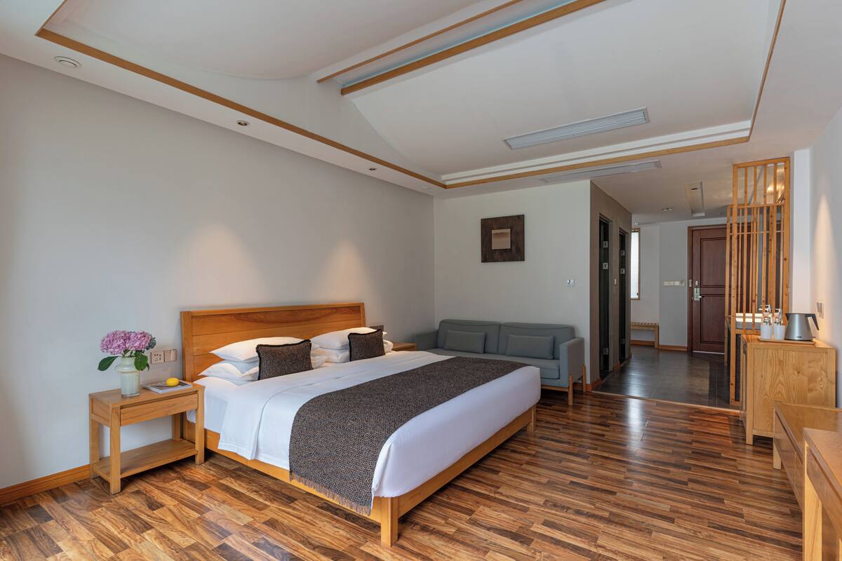 Ein modernes Hotelzimmer mit einem hölzernen Bett, einem Nachttisch, einer Couch und einem Holzschrank.