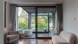 Un interior moderno con un amplio ventanal corredera que da a una piscina, una bañera blanca y un sofá.