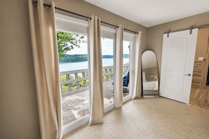 A room with a large sliding glass door leading to a balcony with a view of a lake.