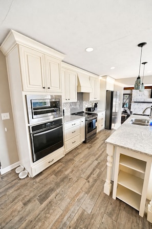A modern kitchen with white cabinetry, stainless steel appliances, and a herringbone wood floor.