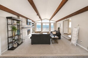 A spacious living room with a fireplace, a large window offering a view, and a high ceiling with exposed beams. - Private Indoor Pool + Slide Sleeps 18+ Lake Cumberland (Somerset)