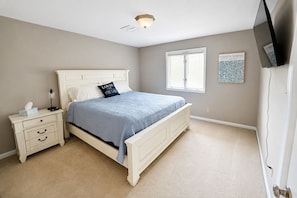 Un dormitorio con cama, mesita de noche, lámpara, decoración en la pared y una ventana.