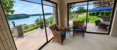 Una terraza con mobiliario de mimbre, vistas a un lago y un patio con sombrillas.