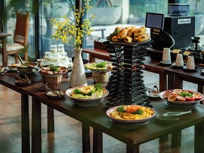 Una mesa de buffet con diversos platos, un jarrón con flores amarillas y una estación de café.