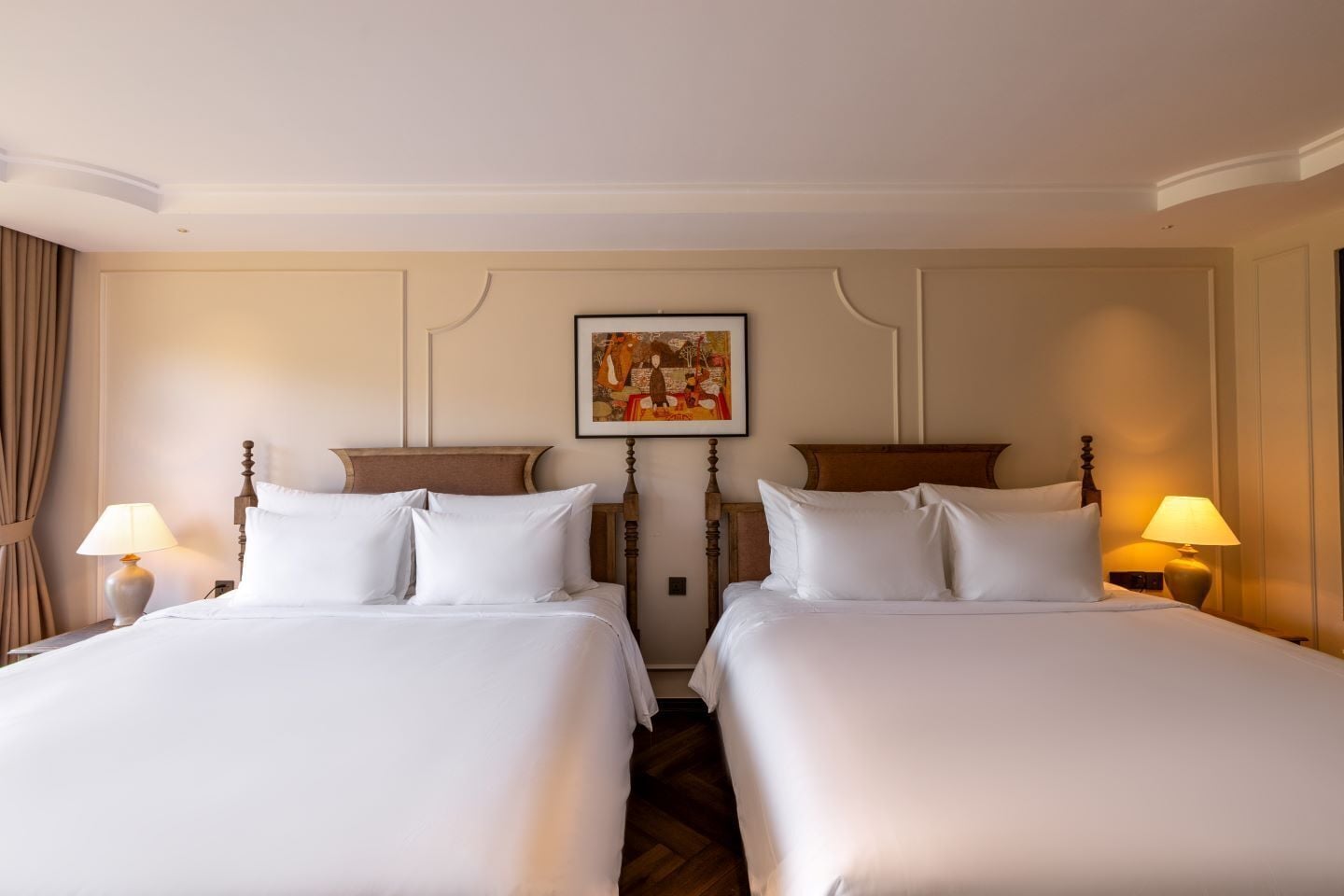 A hotel room with two beds, a painting on the wall, and lamps on either side.