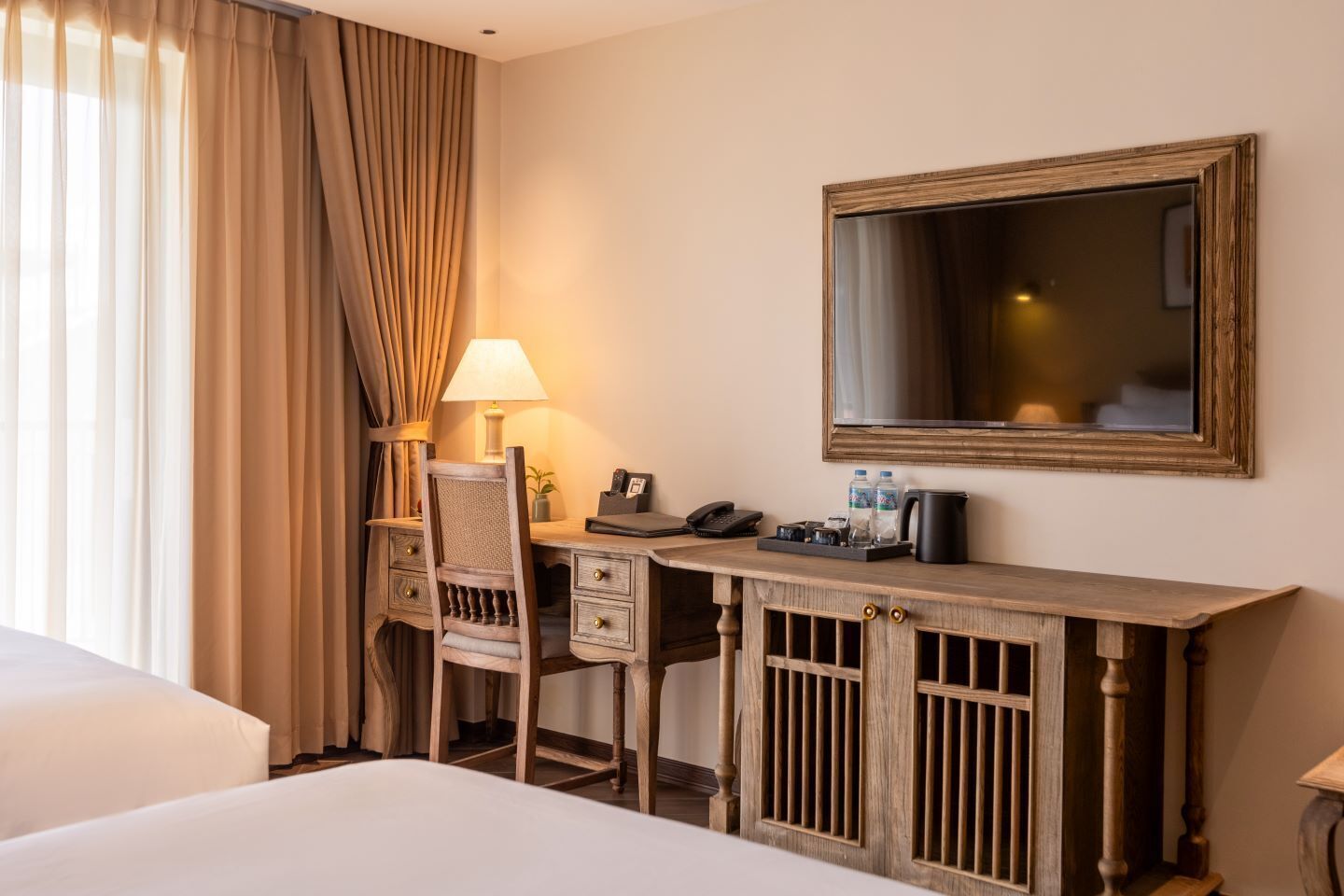 A hotel room with a bed, a desk with a chair, a lamp, a telephone, a coffee maker, and a mirror.