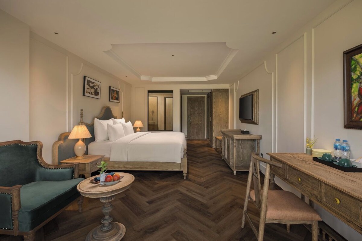 Habitación de hotel con cama, escritorio, silla, una mesa redonda con fruta y televisor.