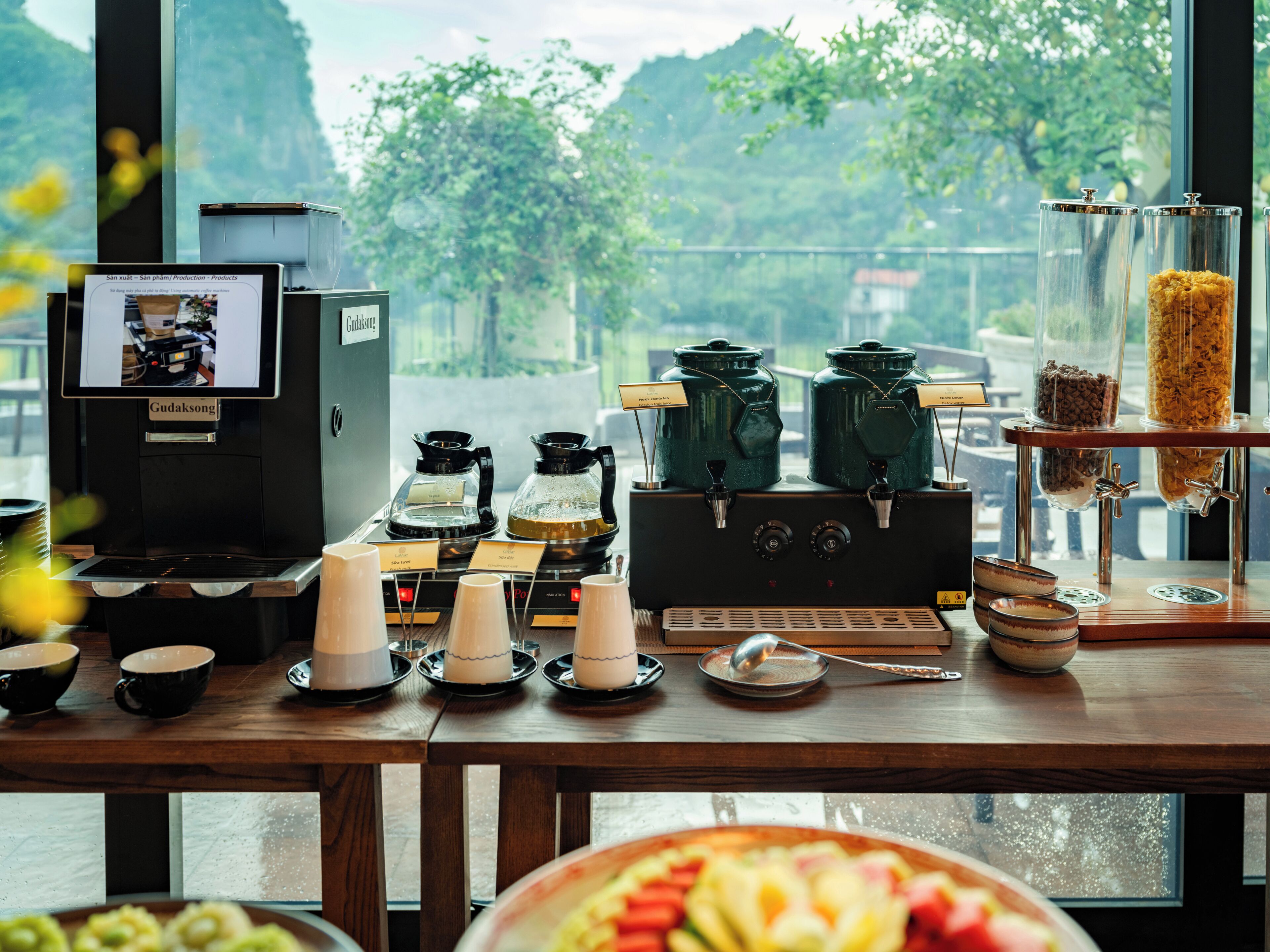 A coffee station with brewing equipment, coffee cups, and a view of greenery outside.