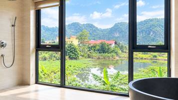 A bathroom with a large window, a shower, and a view of a lake and mountains.