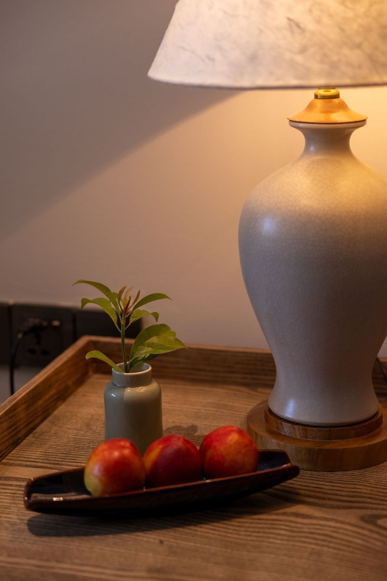 A wooden tray with a vase of green plant and a plate of red apples.