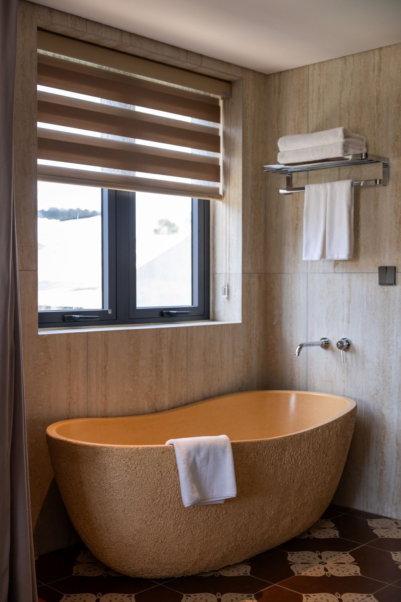 A modern bathroom with a freestanding bathtub, a window with blinds, a towel rack, and a shower area.