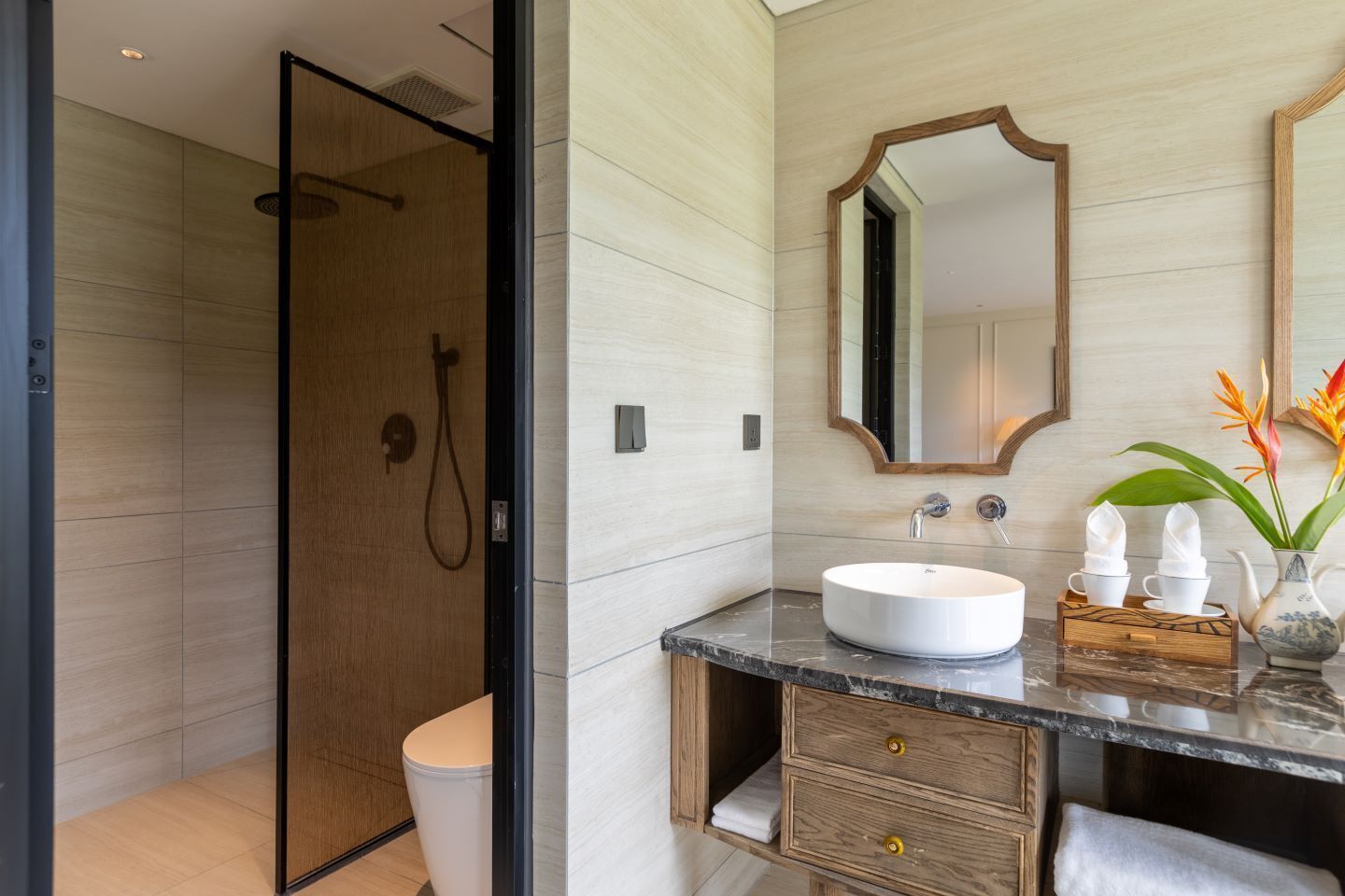 A modern bathroom with a glass-enclosed shower, a white sink, wooden cabinetry, and a mirror with a wooden frame.