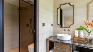 A modern bathroom with a glass-enclosed shower, a white sink, wooden cabinetry, and a mirror with a wooden frame.